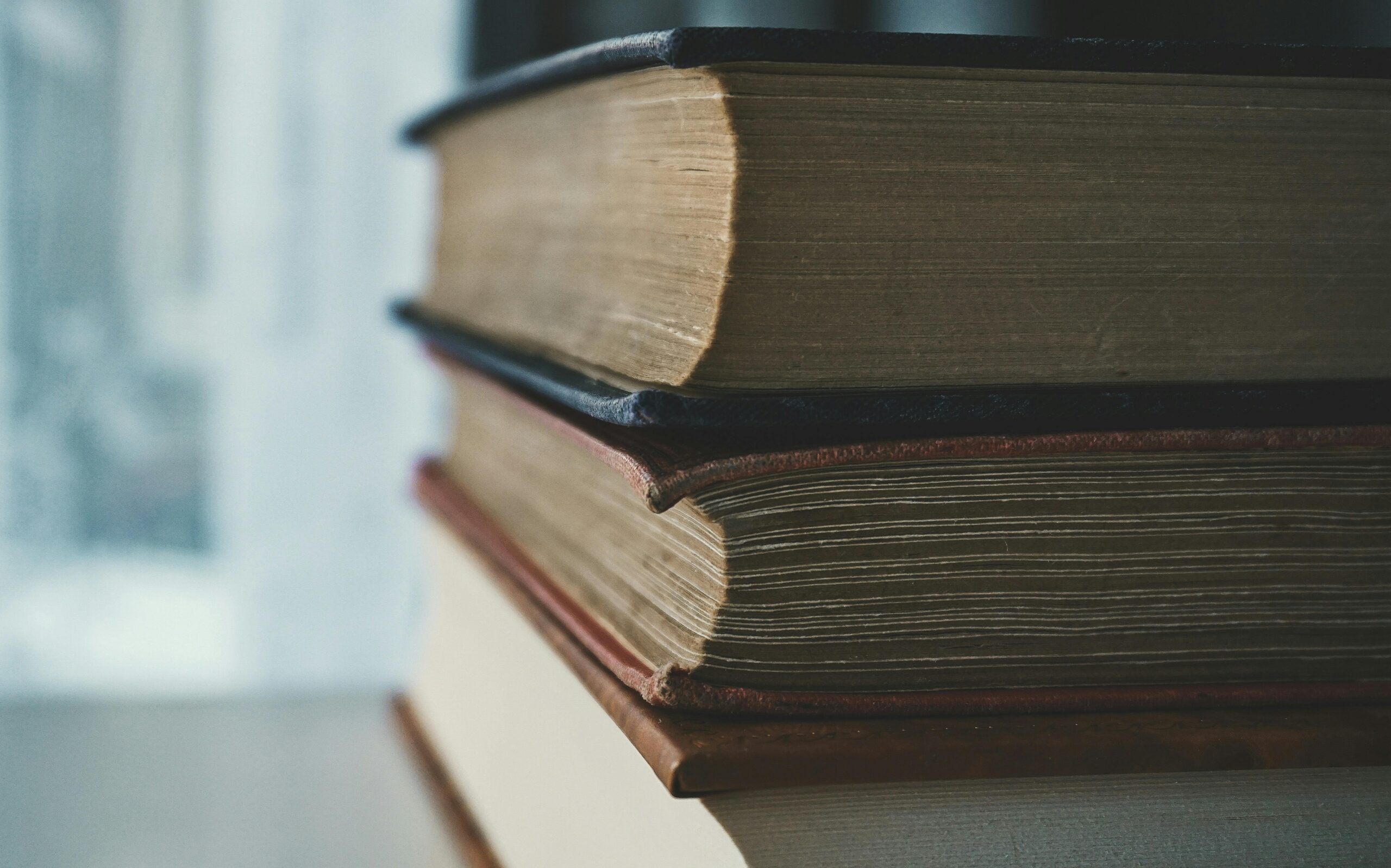 A close-up view of a stack of vintage books with worn pages and covers in soft lighting.